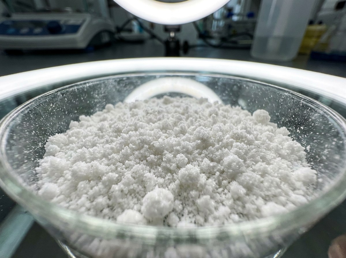 Extreme macro of fine white mineral powder in a small clear glass dish under laboratory light