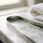 Polished stainless steel U-shaped tongue scraper on a white marble bathroom counter